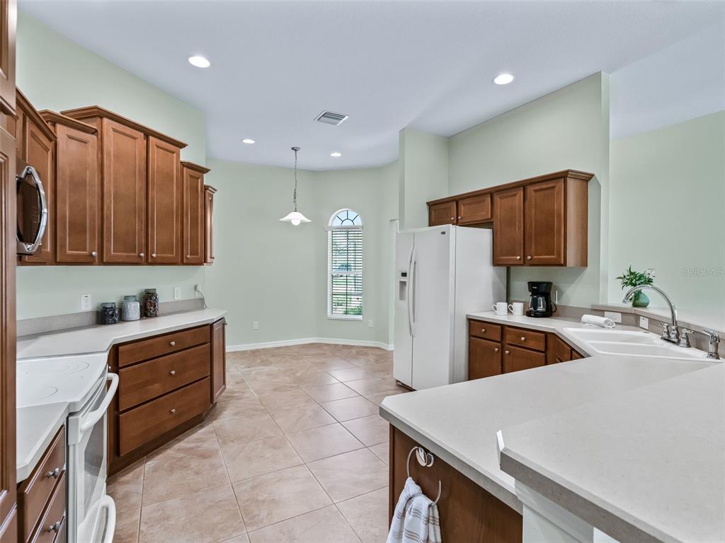 A kitchen features wood cabinets, light countertops, tile flooring, and a dining area with a window — 2215 TRIGGERFISH RUN, THE VILLAGES, FL