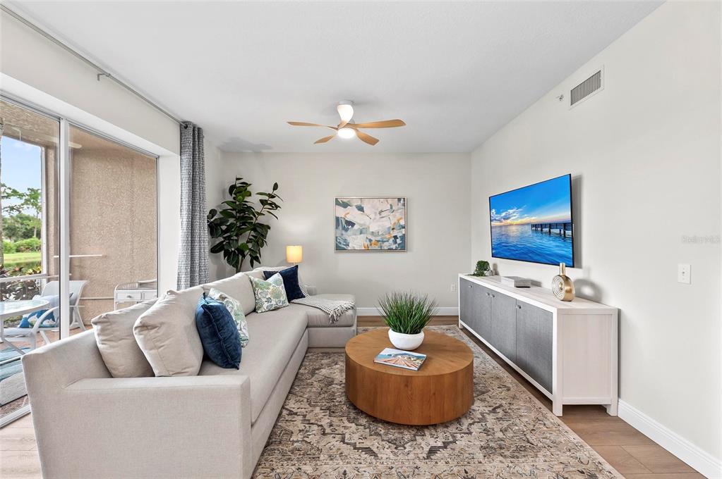 A living room features a sectional sofa, a round wooden coffee table, and a wall-mounted television — 5280 HYLAND HILLS AVENUE UNIT 1812, SARASOTA, FL