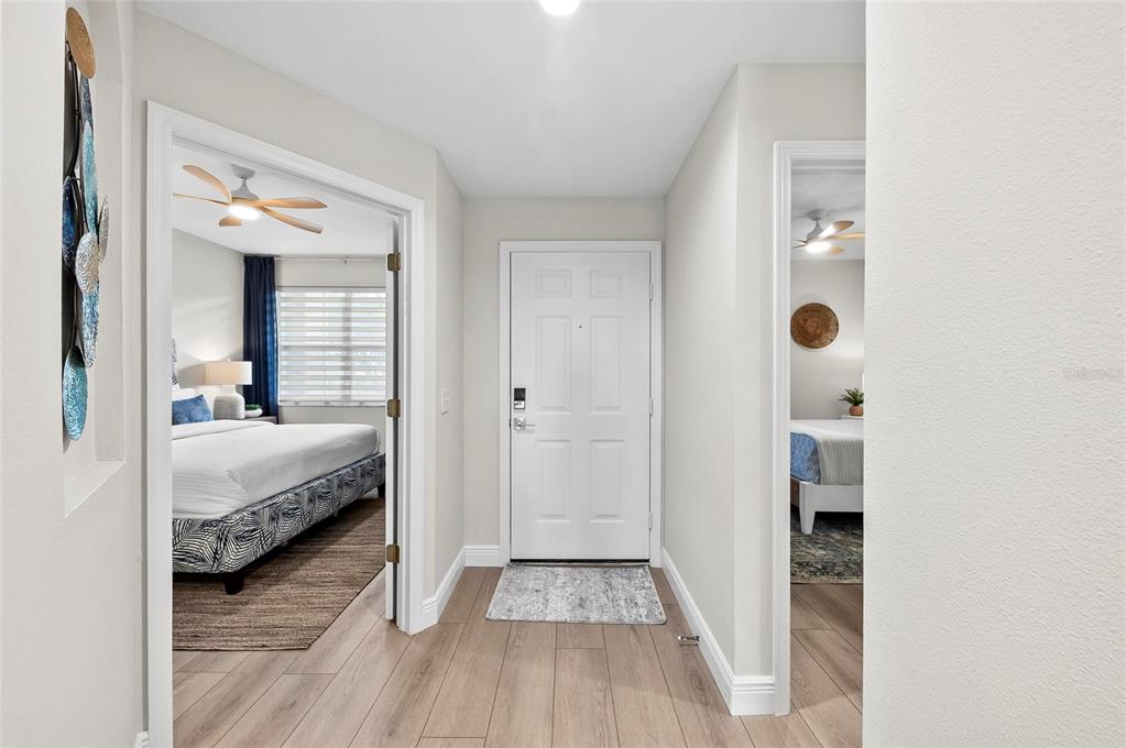A hallway with light wood-look flooring leads to a white front door between two bedrooms — 5280 HYLAND HILLS AVENUE UNIT 1812, SARASOTA, FL