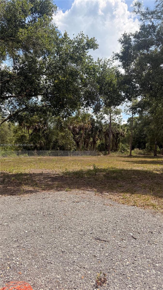 A gravel driveway leads to a cleared, grassy lot bordered by mature trees and fencing — 465 S Estribo st, Clewiston FL 33440-2613, CLEWISTON, FL