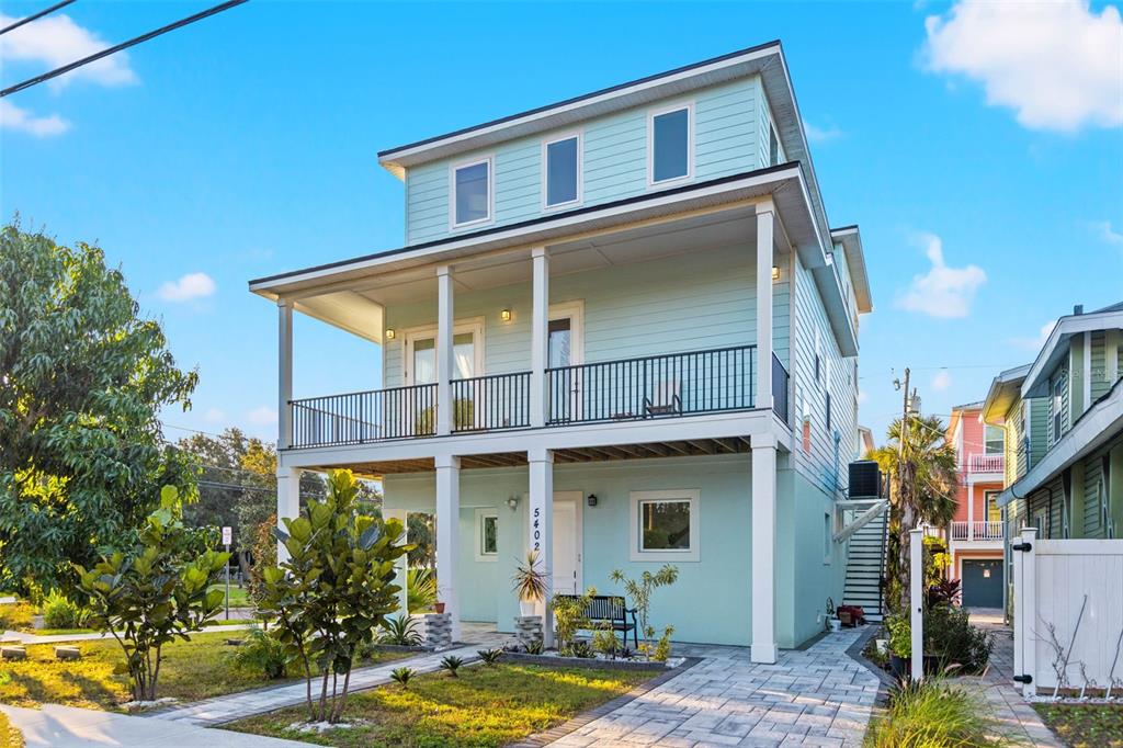 A light blue, three-story stilt house with a front porch and a paved driveway — 5402 31ST AVENUE S, GULFPORT, FL