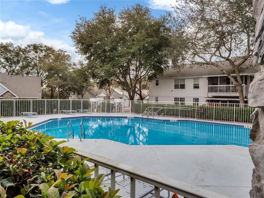 A swimming pool with a white fence is surrounded by trees and apartment buildings — 930 LOCH CARRON UNIT 1212, APOPKA, FL