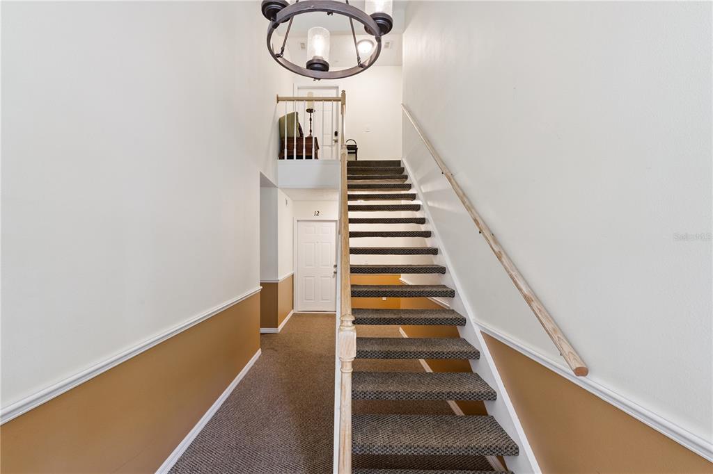 An interior view shows a carpeted staircase leading to an upper landing with a chandelier — 930 LOCH CARRON UNIT 1212, APOPKA, FL
