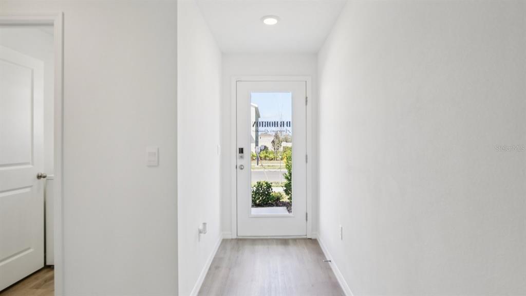 A bright entryway features light wood-look flooring, white walls, and a glass-paneled front door — 13484 SUMMIT PEAK COURT, DADE CITY, FL