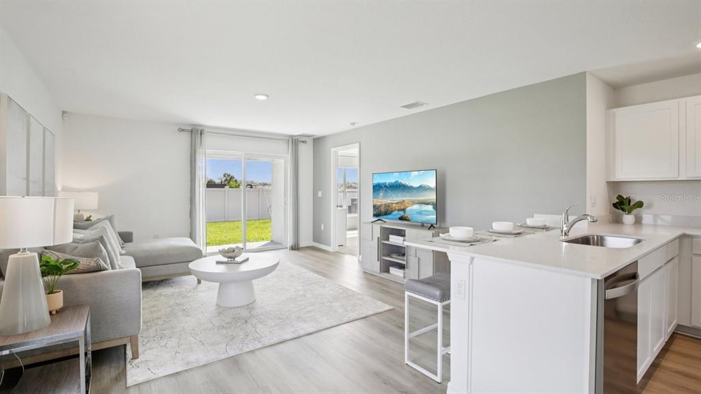 An open-concept living room and kitchen featuring light wood flooring, white cabinetry, and a sliding door — 13484 SUMMIT PEAK COURT, DADE CITY, FL