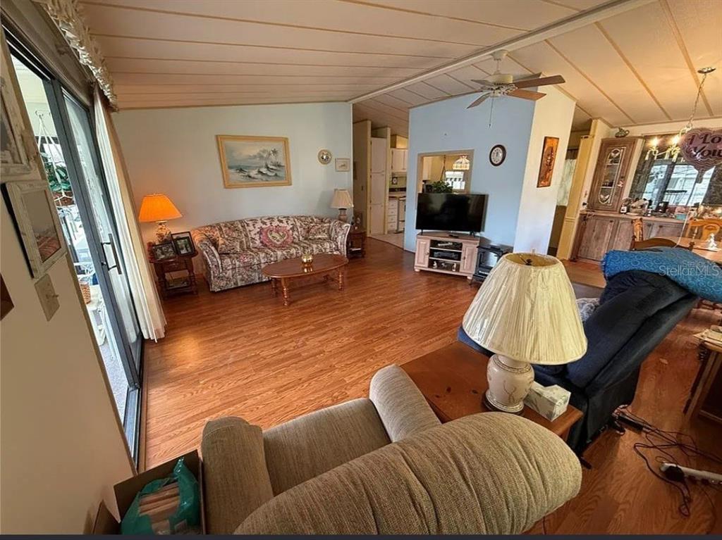 A living room features wood-look flooring, a floral sofa, a television, and a ceiling fan — 1532 W SCHWARTZ BOULEVARD, LADY LAKE, FL