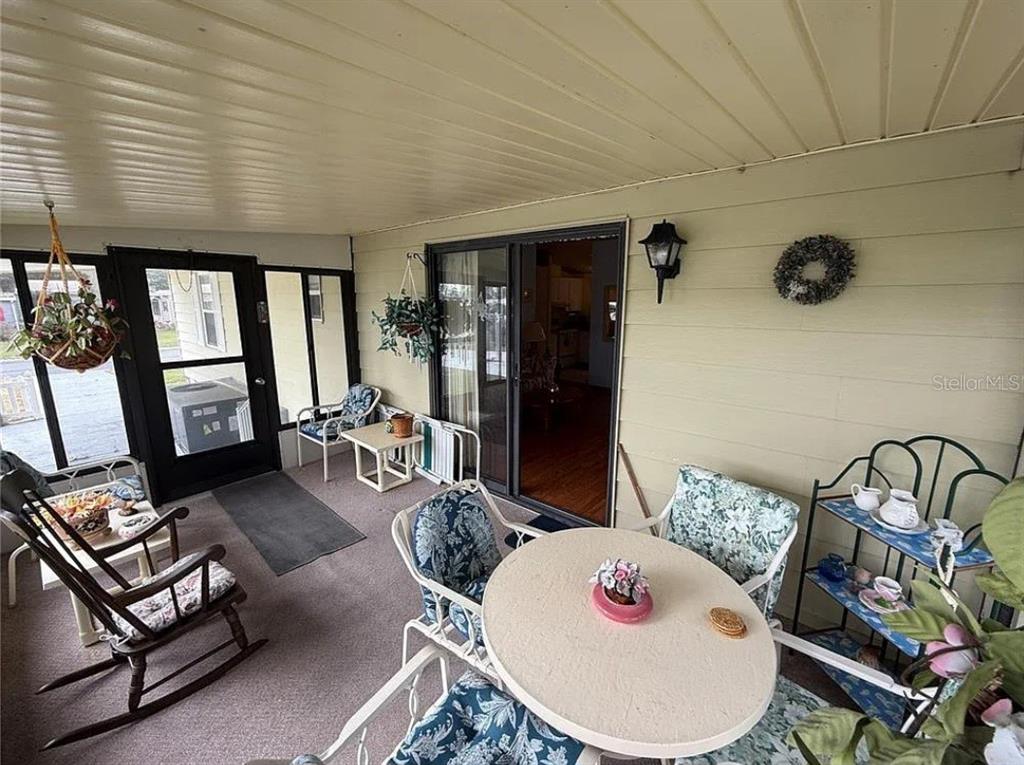 A covered patio features a round table, rocking chairs, and a sliding glass door entrance — 1532 W SCHWARTZ BOULEVARD, LADY LAKE, FL