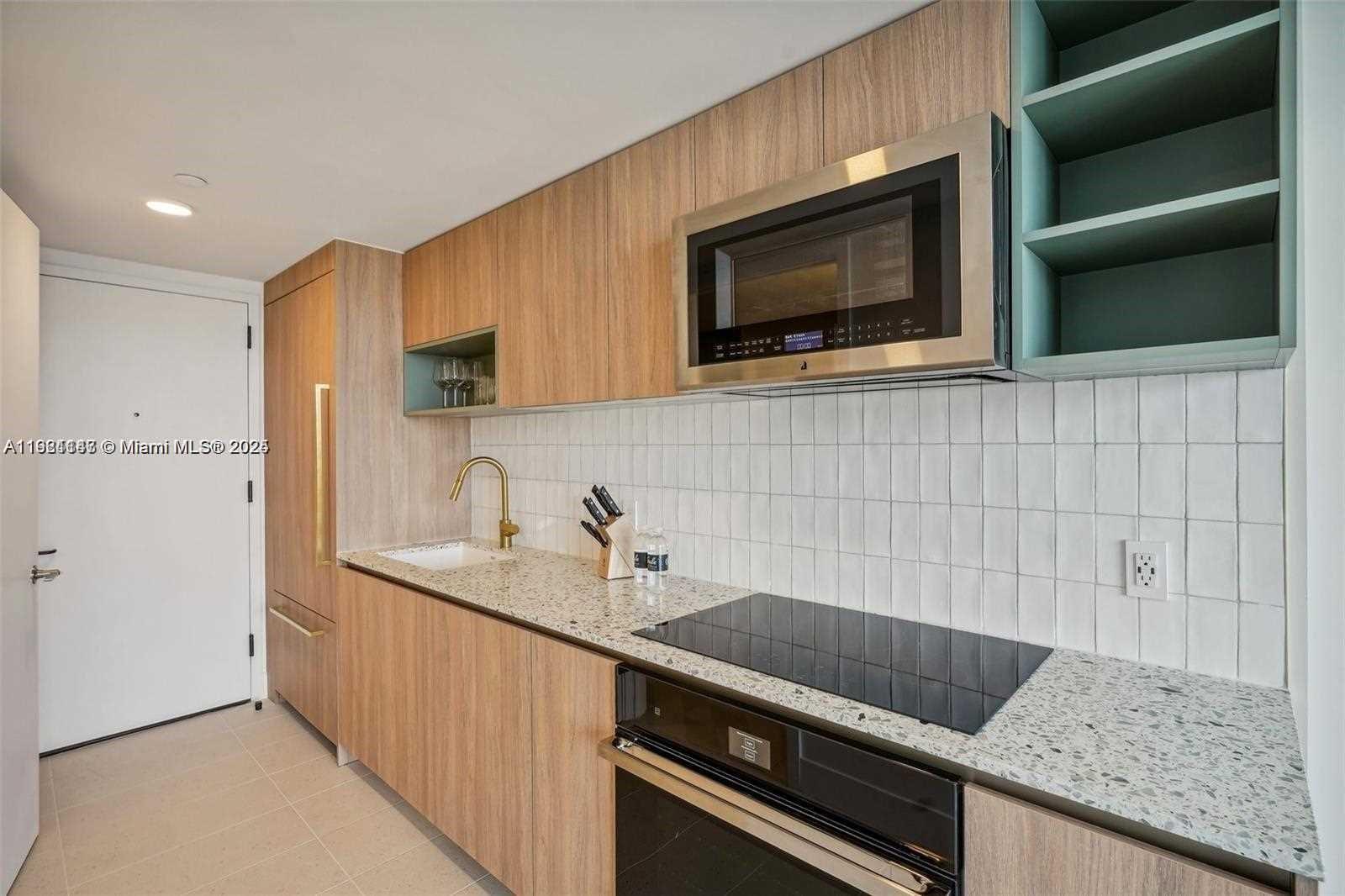 A modern kitchen features wood-grain cabinetry, a speckled countertop, a white tile backsplash, and appliances — 159 NE 6th St # 4114, Miami FL 33132, MIAMI, FL