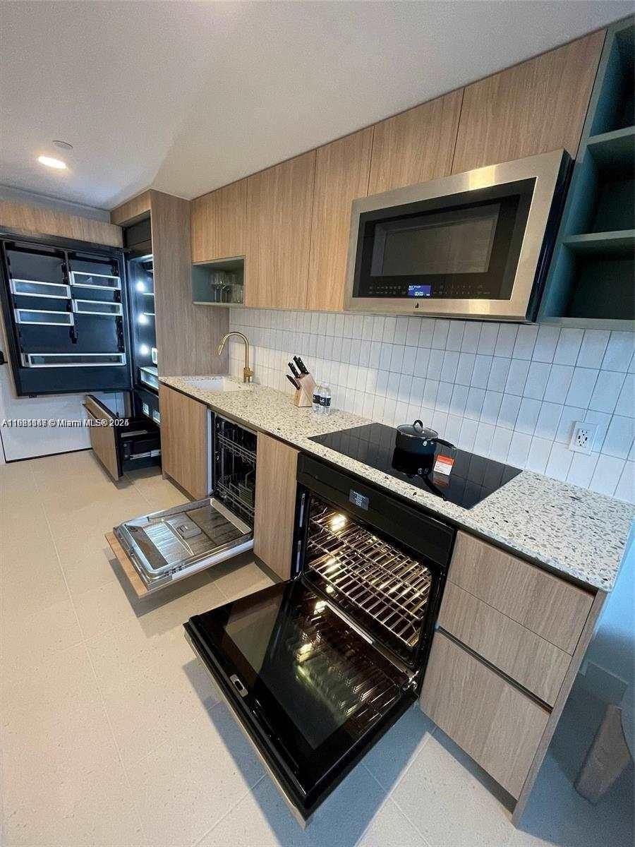 A modern kitchen features light wood cabinetry, granite countertops, stainless steel appliances, and white tile — 159 NE 6th St # 4114, Miami FL 33132, MIAMI, FL