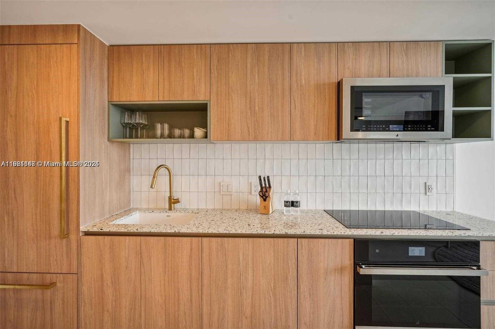 A modern kitchen features wood-grain cabinets, a speckled countertop, and a white tiled backsplash — 159 NE 6th St # 4114, Miami FL 33132, MIAMI, FL