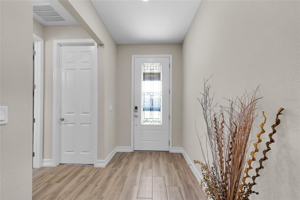 A bright entryway features light wood-look tile flooring, a white front door, and beige walls — 4394 NW 54TH TERRACE, OCALA, FL