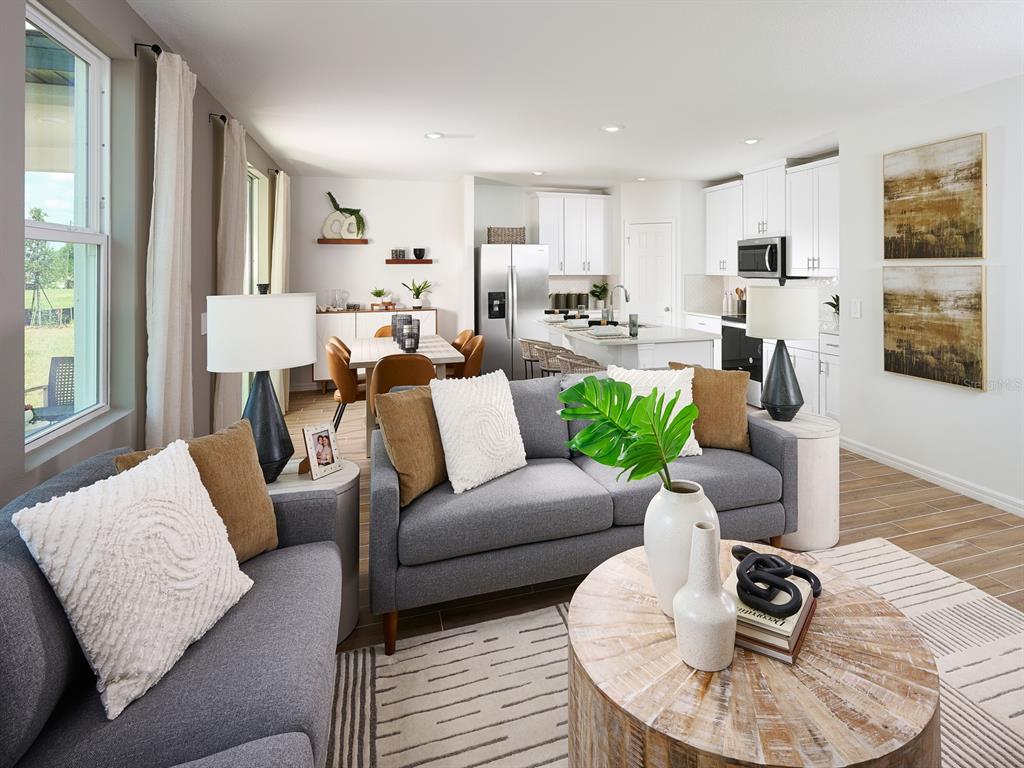 A living room with gray sofas and a coffee table opens to a dining area and kitchen — 706 IMPALA ROAD, LAKE ALFRED, FL