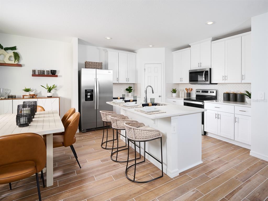 A bright kitchen features white cabinetry, a central island with bar stools, and wood-look flooring — 706 IMPALA ROAD, LAKE ALFRED, FL