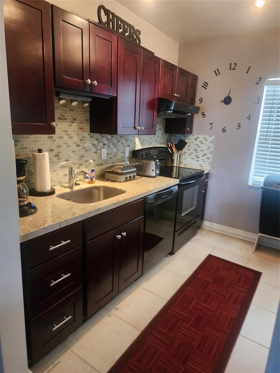A kitchen features dark wood cabinets, granite countertops, a tiled backsplash, and a wall clock — 7500 NW 4th Place, Margate FL 33063, MARGATE, FL