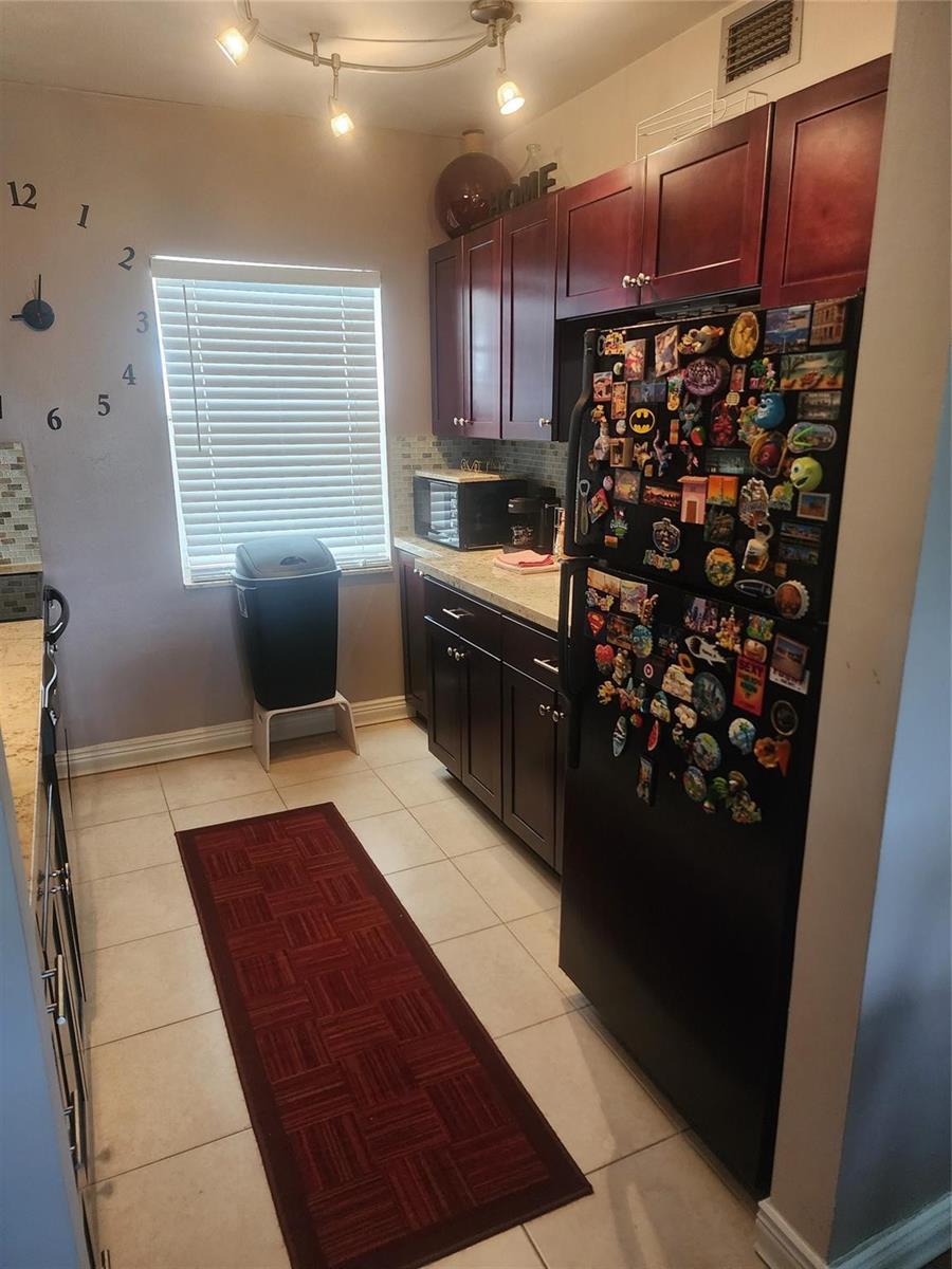 A kitchen features dark wood cabinets, a black refrigerator covered in magnets, and tile flooring — 7500 NW 4th Place, Margate FL 33063, MARGATE, FL