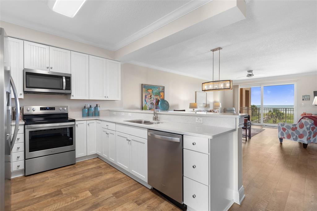 A kitchen with white cabinets, stainless steel appliances, and a breakfast bar overlooking the living area — 60 SURFVIEW DRIVE UNIT 214, PALM COAST, FL