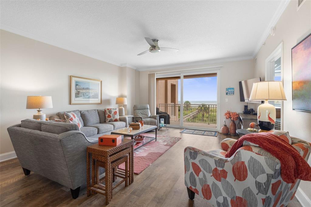A living room features a grey sofa, patterned armchair, and sliding doors opening to a balcony — 60 SURFVIEW DRIVE UNIT 214, PALM COAST, FL