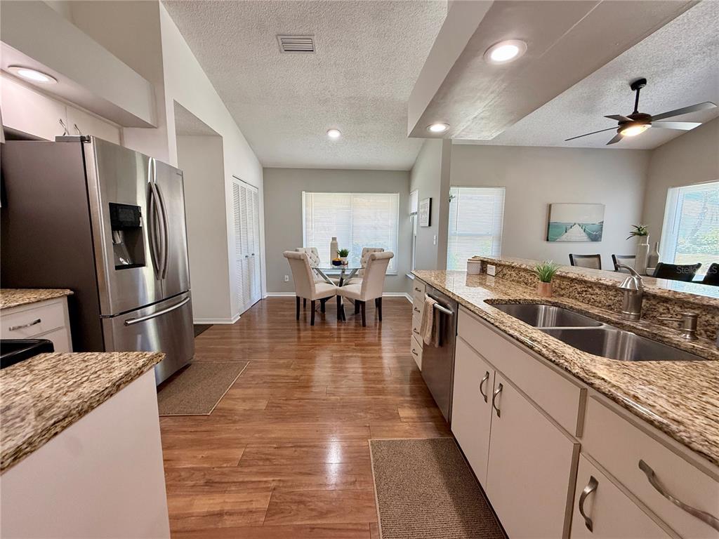 A kitchen with granite countertops and stainless steel appliances overlooks a dining area with wood floors — 1603 E DEL WEBB BOULEVARD, SUN CITY CENTER, FL