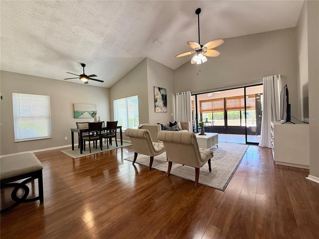 An open-concept living and dining area features hardwood floors, vaulted ceilings, and a sliding glass door — 1603 E DEL WEBB BOULEVARD, SUN CITY CENTER, FL