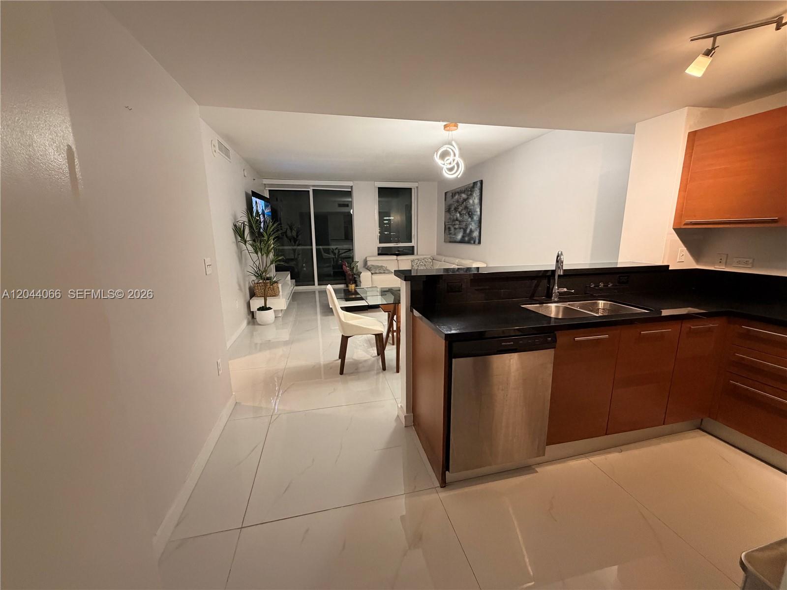 A modern kitchen with dark countertops and wood cabinets overlooks an open-concept living area — 253 NE 2nd St # 1204, Miami FL 33132, MIAMI, FL