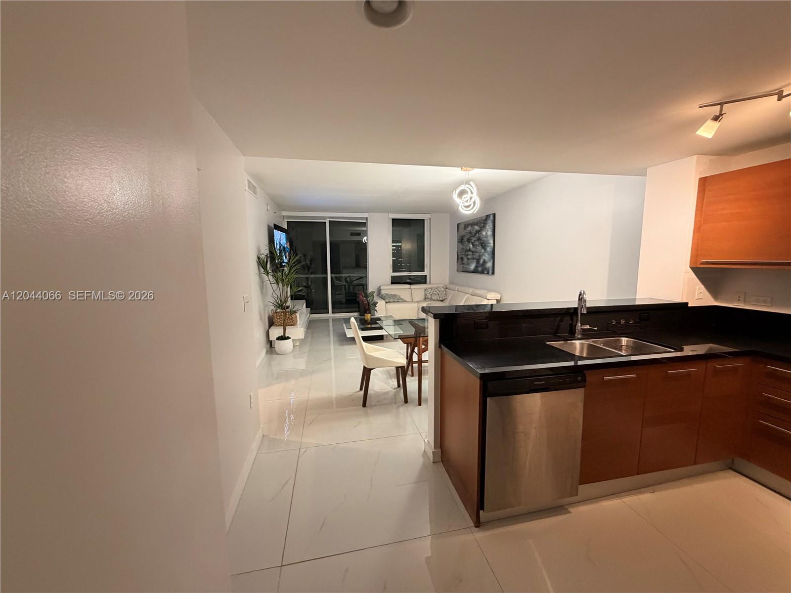 A kitchen with dark countertops and wood cabinets overlooks an open-concept living and dining area — 253 NE 2nd St # 1204, Miami FL 33132, MIAMI, FL