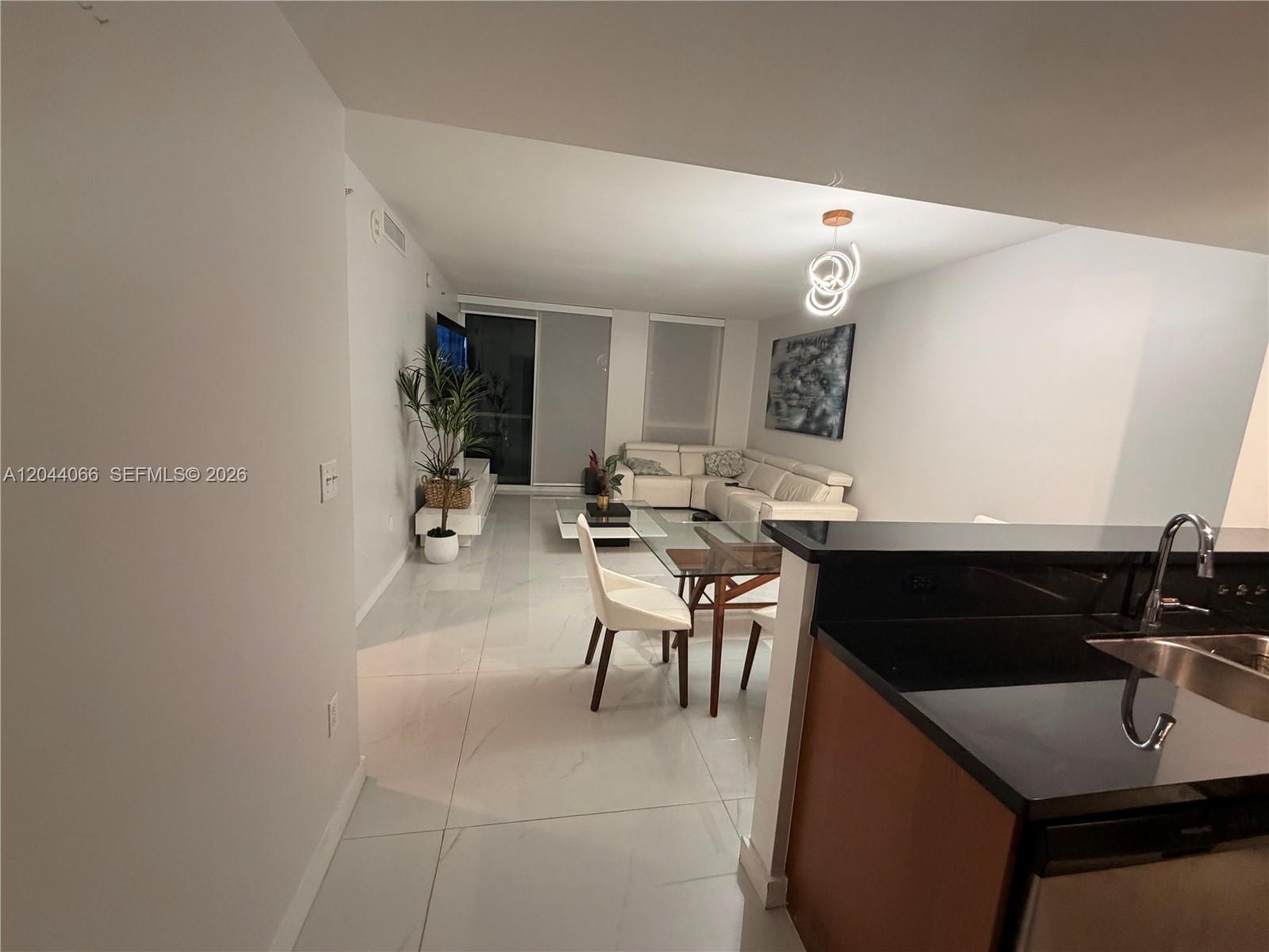 A modern living and dining area features white tile floors, a sectional sofa, and kitchen — 253 NE 2nd St # 1204, Miami FL 33132, MIAMI, FL