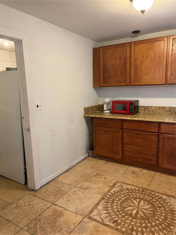 A kitchen features wooden cabinets, a granite countertop, a red microwave, and tiled flooring — 915 WINCHESTER STREET, DAYTONA BEACH, FL