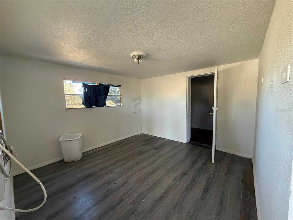 An empty room with white walls, gray wood-look flooring, a window, and an open doorway — 9013 BURR DRIVE, POLK CITY, FL