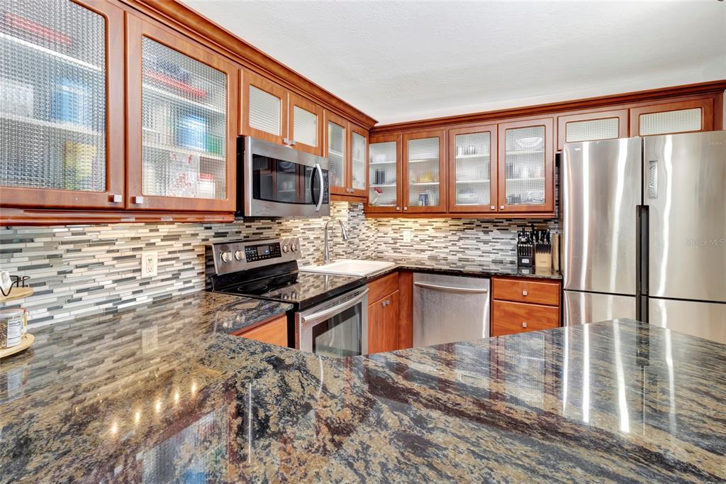 A kitchen features wood cabinets with glass-paneled doors, granite countertops, and stainless steel appliances — 400 E COLONIAL DRIVE UNIT 1609, ORLANDO, FL