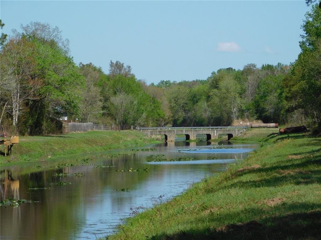 A concrete bridge spans a narrow canal surrounded by grassy banks and dense green trees — 10505 E DEEP CREEK BOULEVARD, HASTINGS, FL