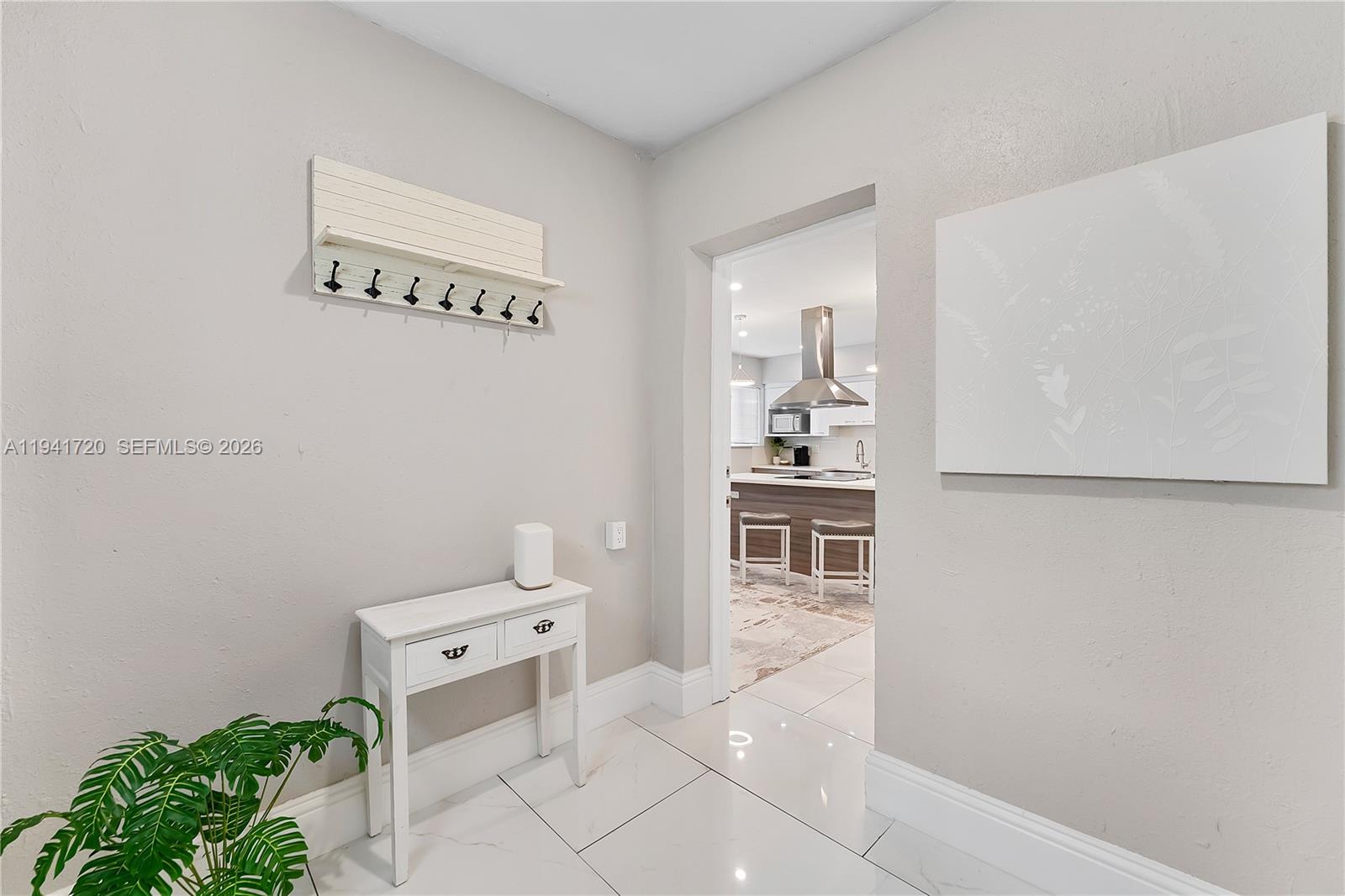A white console table and coat rack sit in a hallway leading to a kitchen — 2227 Cody St, Hollywood FL 33020, HOLLYWOOD, FL