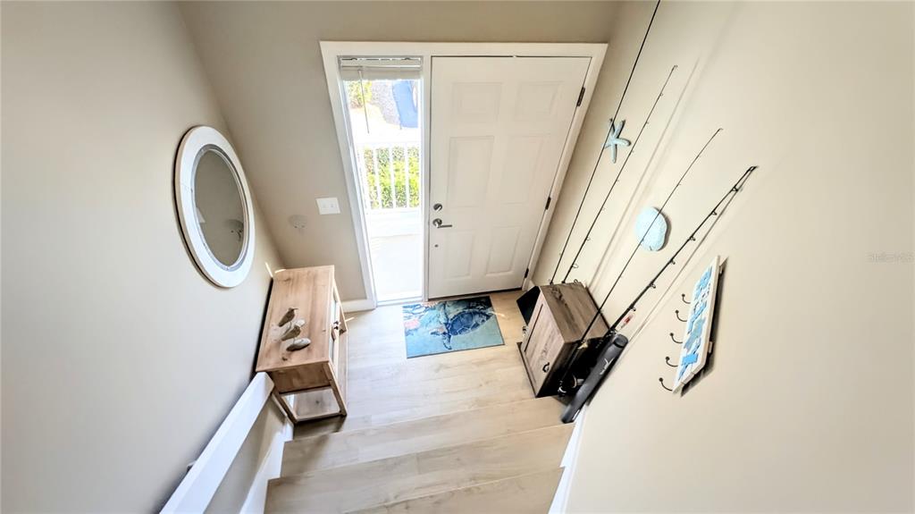 An entryway with light wood stairs, a white door, a round mirror, and fishing rods — 958 SANDPIPER CIRCLE UNIT 958, BRADENTON, FL