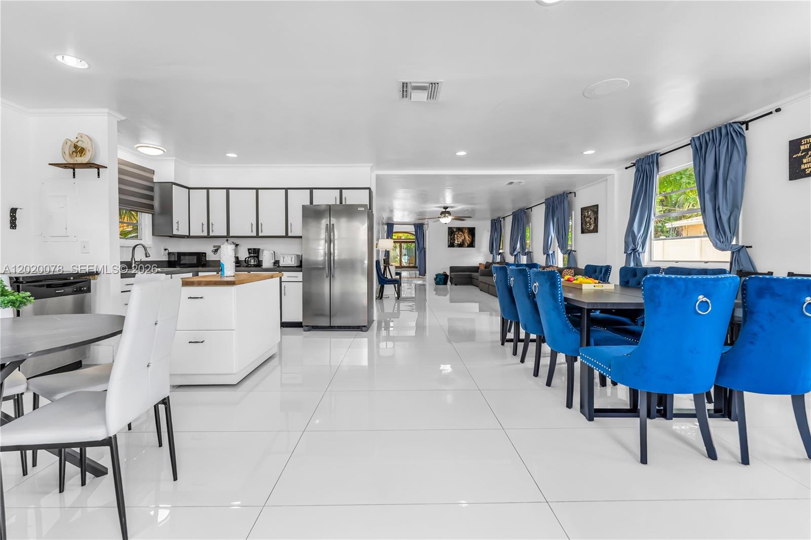 An open-concept kitchen and dining area features white cabinetry, stainless steel appliances, and blue chairs — 1738 N 16th Ct, Hollywood FL 33020, HOLLYWOOD, FL