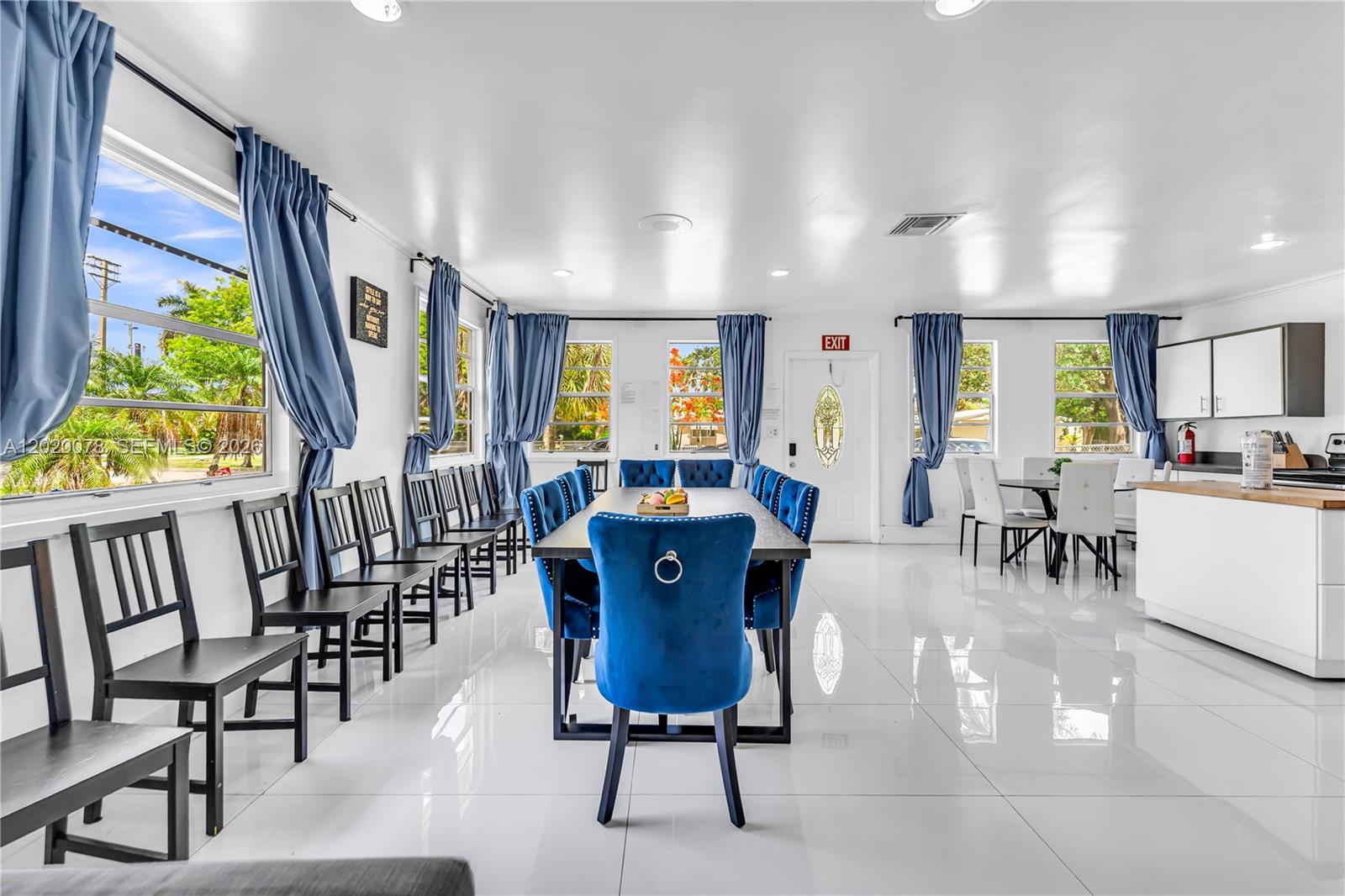 A dining room features a long table with blue velvet chairs, white floors, and windows — 1738 N 16th Ct, Hollywood FL 33020, HOLLYWOOD, FL