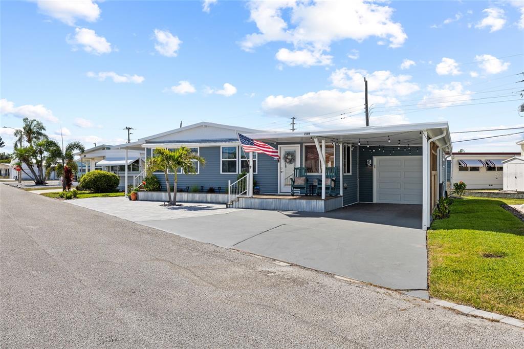 A blue manufactured home features a front porch, an American flag, and a paved carport — 2109 OHIO AVENUE, BRADENTON, FL
