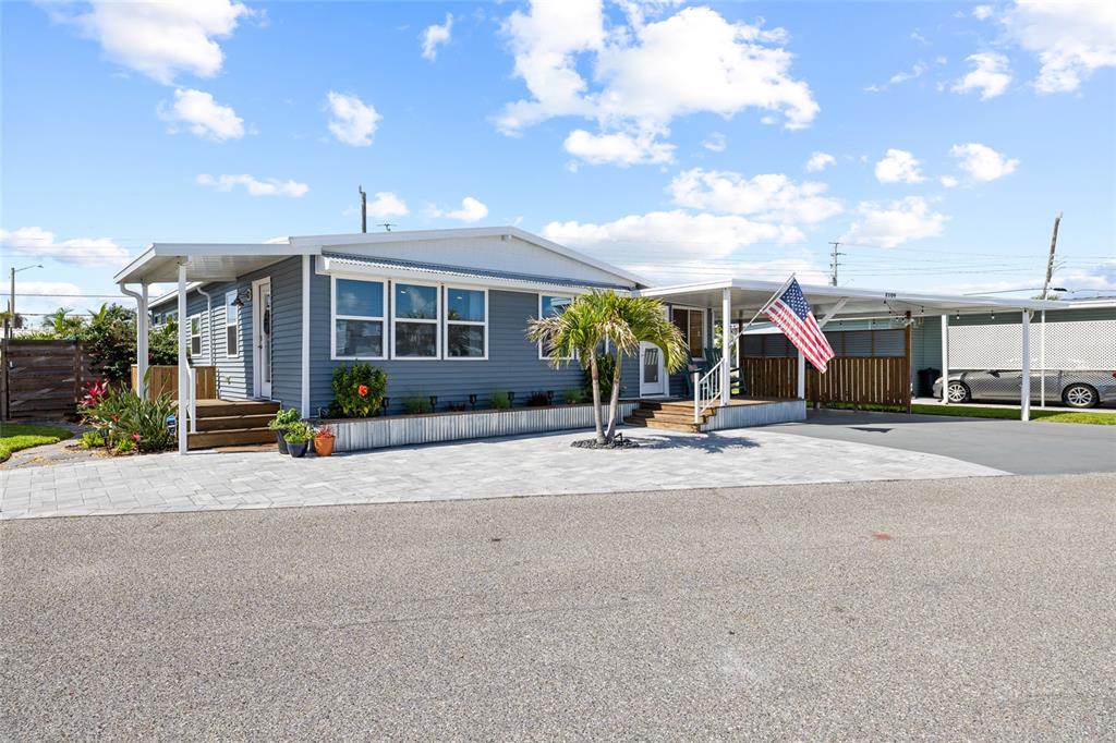 A blue manufactured home features a paved driveway, a carport, and an American flag — 2109 OHIO AVENUE, BRADENTON, FL