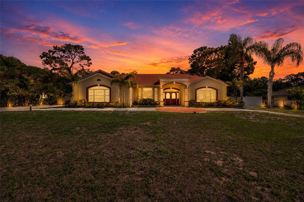 A single-story house with a tan exterior and arched windows stands under a sunset sky — 6341 GOVERNORS DRIVE, NEW PORT RICHEY, FL