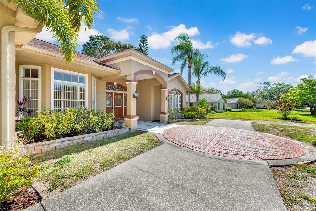 The exterior of a tan house features a circular brick driveway and a covered entryway — 6341 GOVERNORS DRIVE, NEW PORT RICHEY, FL