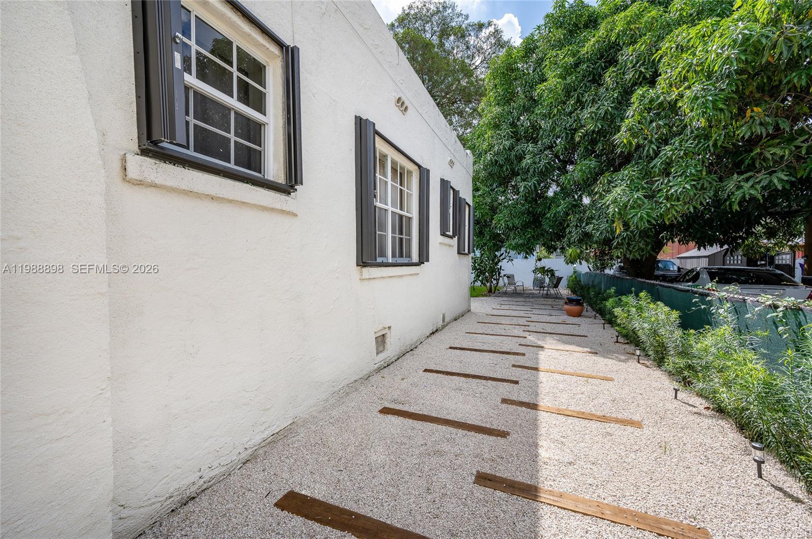 A white stucco house exterior features dark shutters, gravel landscaping, and wooden walkway planks — 1844 NW 47th St, Miami FL 33142, MIAMI, FL