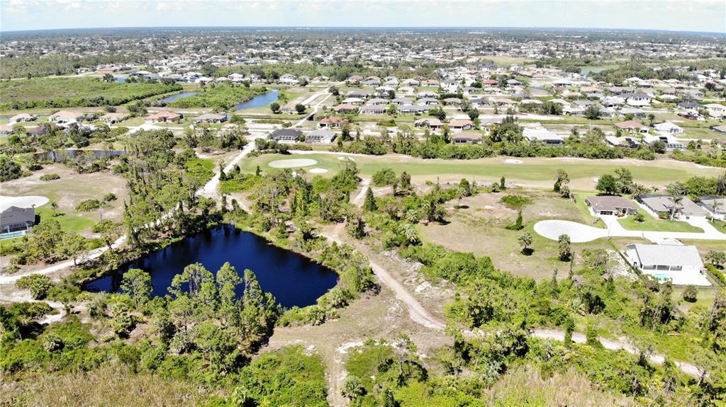 An aerial view shows a pond, undeveloped land, and a golf course near residential homes — 89 PINE VALLEY PLACE, ROTONDA WEST, FL