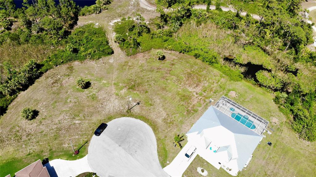 An aerial view shows a house with a pool cage situated on a large corner lot — 89 PINE VALLEY PLACE, ROTONDA WEST, FL