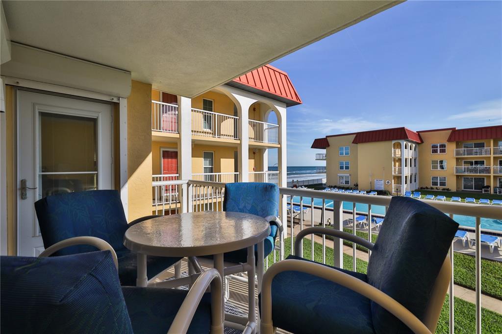 A balcony with a table and chairs overlooks a swimming pool and the ocean — 3801 S ATLANTIC AVENUE UNIT UT204, NEW SMYRNA BEACH, FL