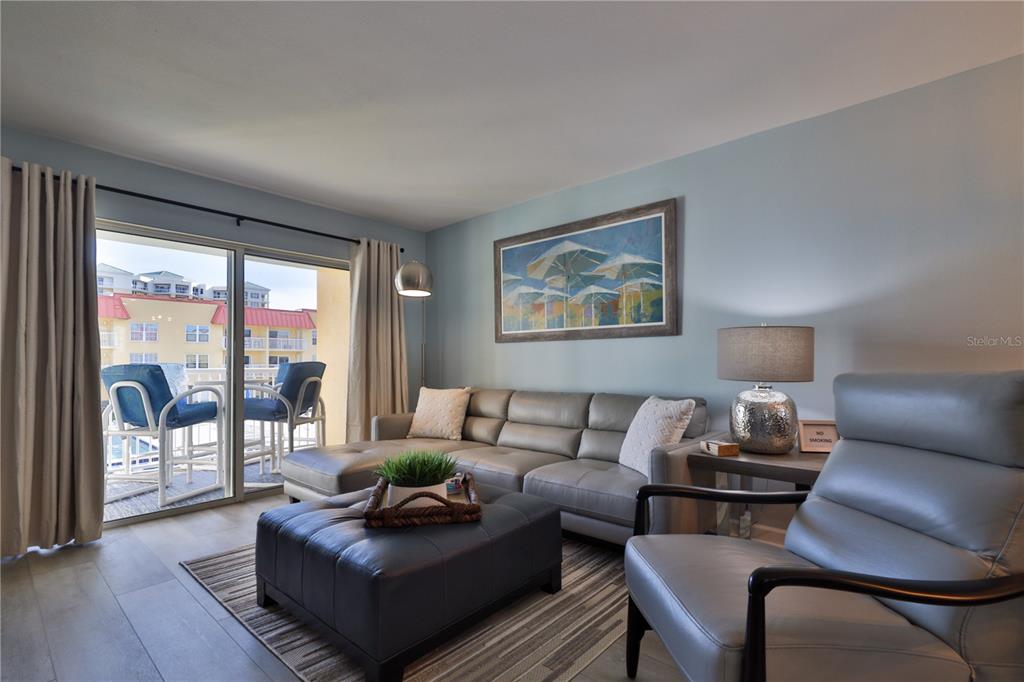 A living room features a gray sectional sofa, leather ottoman, and sliding doors to a balcony — 3801 S ATLANTIC AVENUE UNIT UT204, NEW SMYRNA BEACH, FL