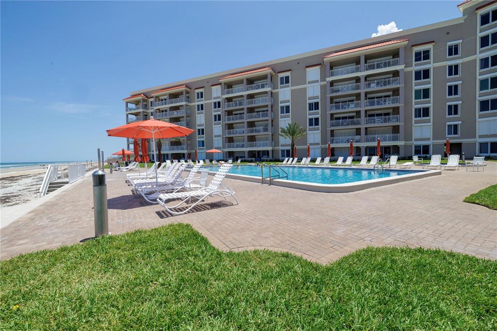 A multi-story beachfront resort building features a swimming pool, lounge chairs, and umbrellas — 5501 ATLANTIC UNIT 107, NEW SMYRNA BEACH, FL