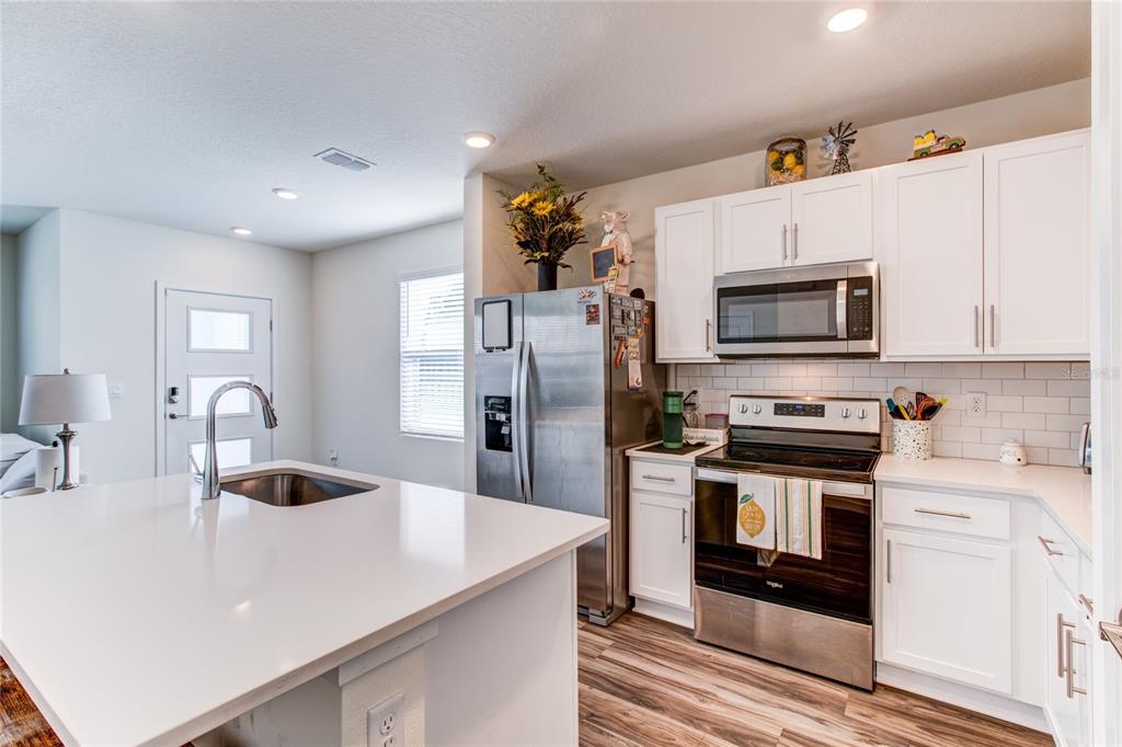A modern kitchen features white cabinetry, stainless steel appliances, and a large quartz-topped island — 214 E CHURCH AVENUE, LONGWOOD, FL