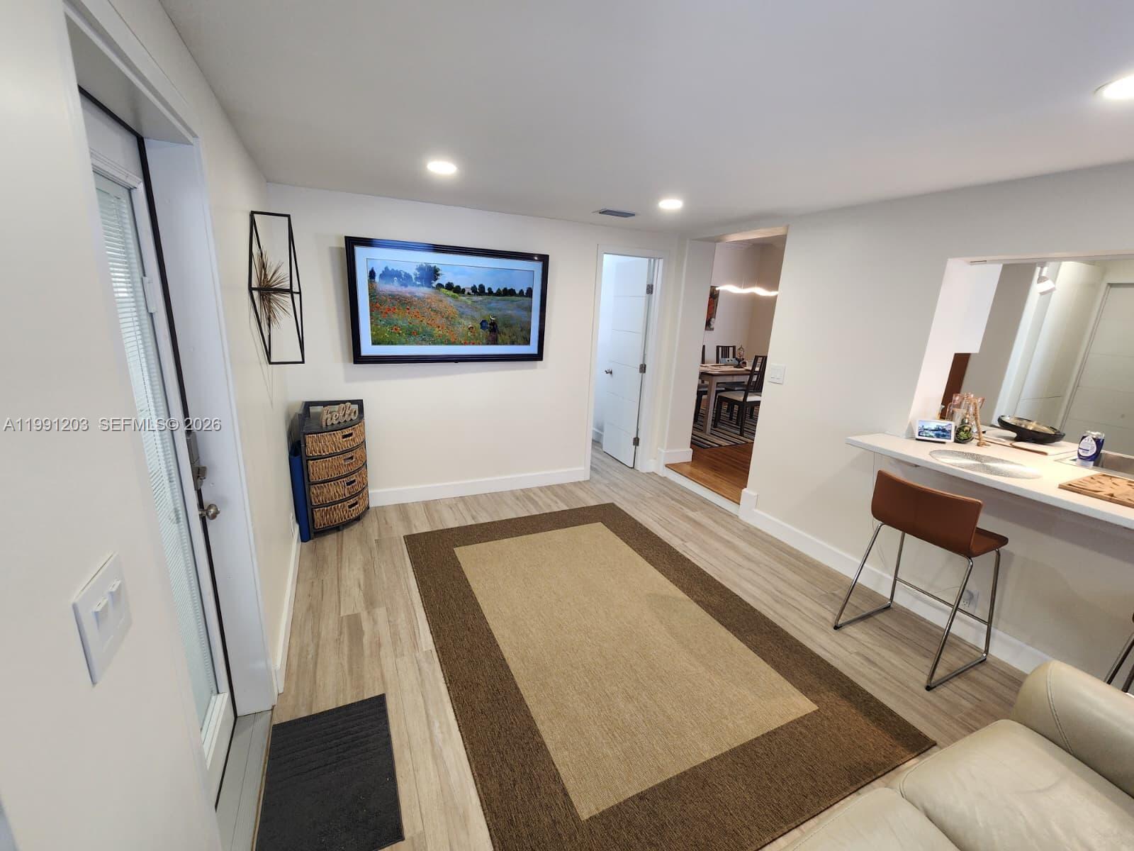This living area features light wood-look flooring, a large area rug, and a breakfast bar — 831 Plover Ave, Miami Springs FL 33166, MIAMI SPRINGS, FL