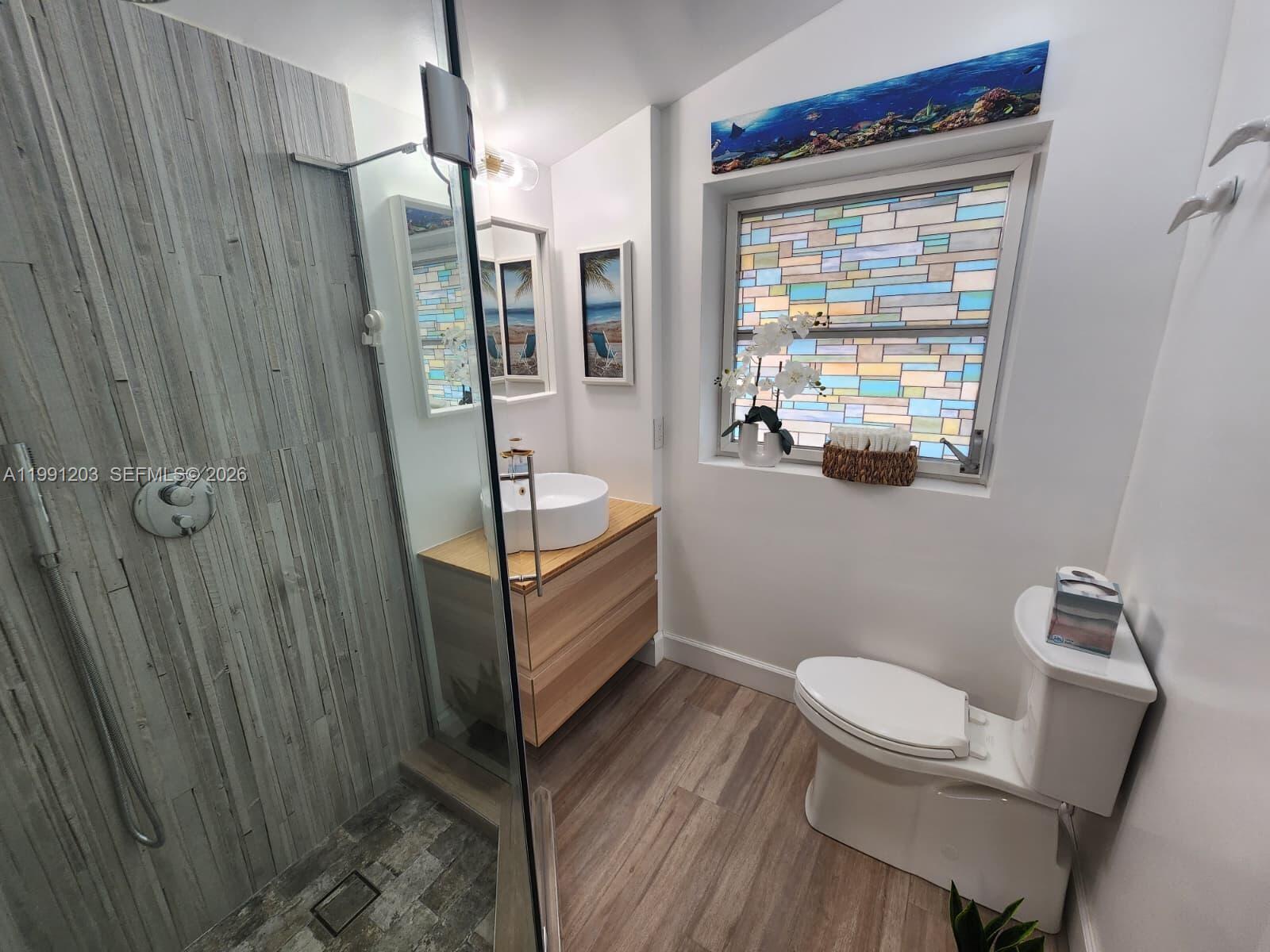 A modern bathroom features a glass-enclosed shower, wood-look vanity, and a stained-glass window — 831 Plover Ave, Miami Springs FL 33166, MIAMI SPRINGS, FL