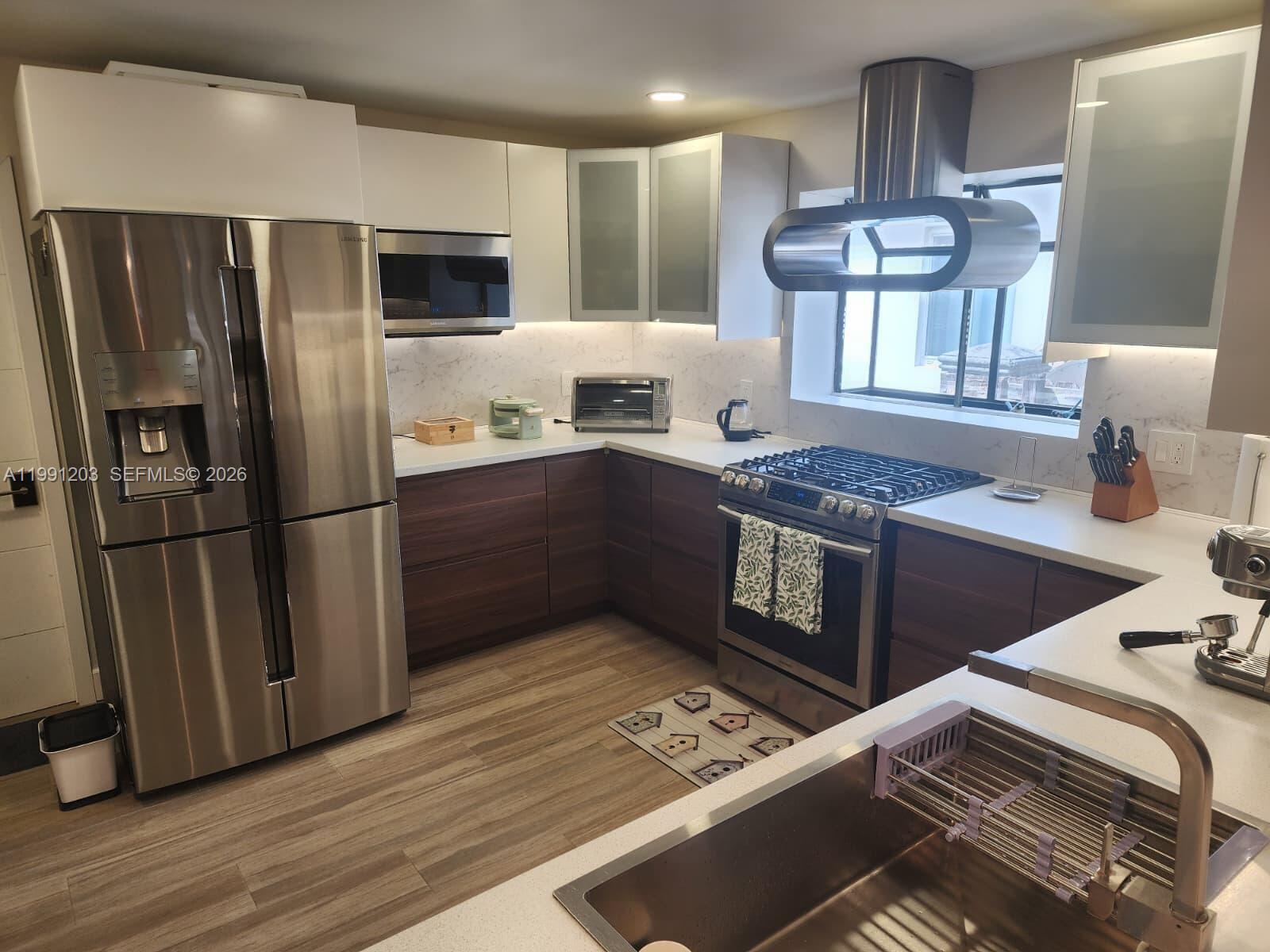 A modern kitchen features stainless steel appliances, two-toned cabinetry, and white countertops — 831 Plover Ave, Miami Springs FL 33166, MIAMI SPRINGS, FL
