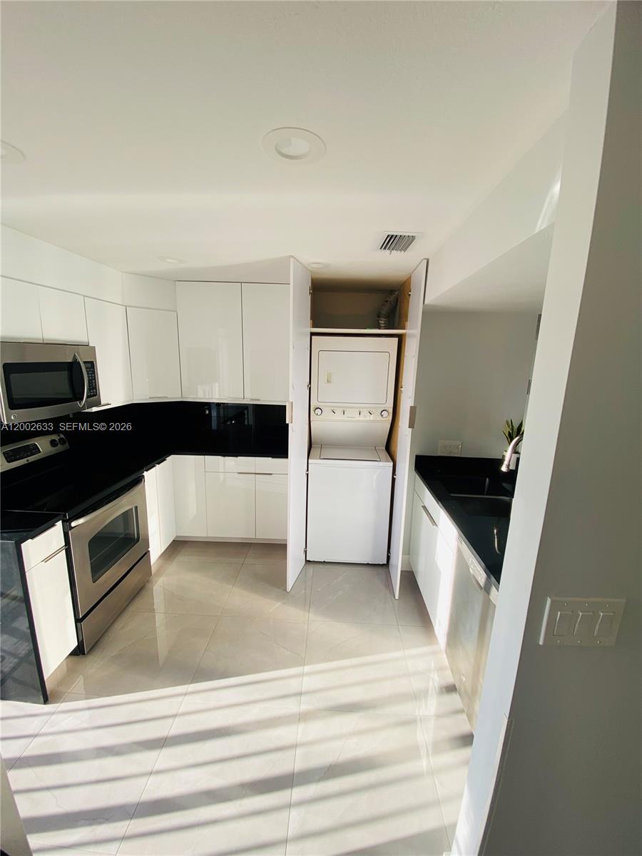 A modern kitchen features white cabinets, black countertops, stainless steel appliances, and an integrated laundry unit — 199 SW 12th Ave # C, Miami FL 33130, MIAMI, FL
