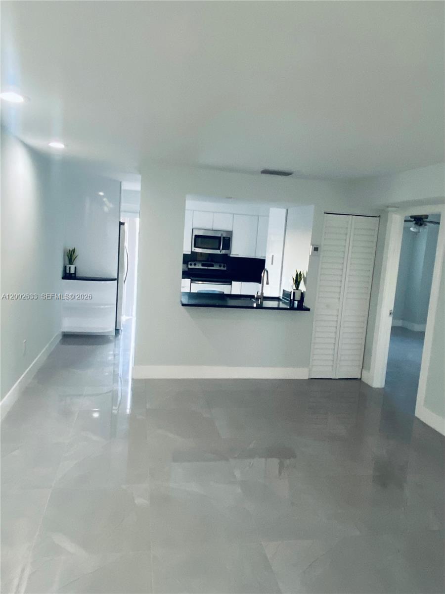 A living area with light gray tile flooring leads to a kitchen with a pass-through window — 199 SW 12th Ave # C, Miami FL 33130, MIAMI, FL